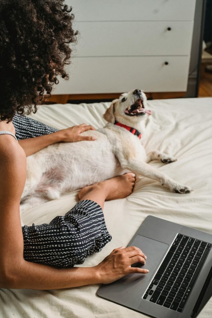 A woman enjoys a relaxing moment with her pet dog while using a laptop at home, portraying leisure and companionship.